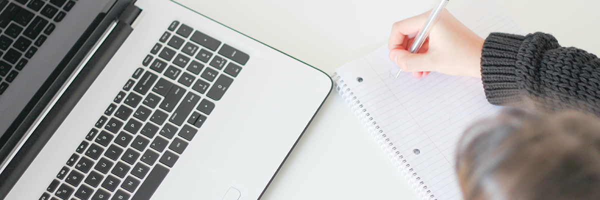 Girl writing notes as she looks at a laptop