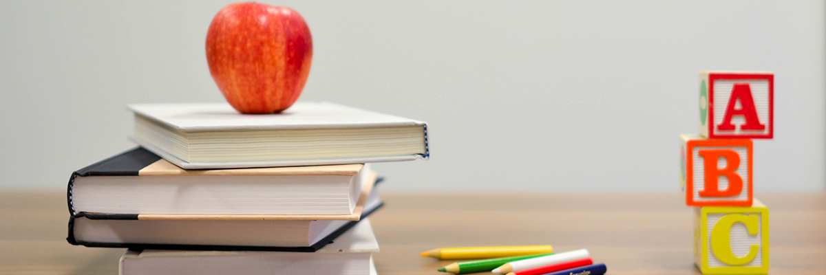 Apple placed on a stack of books next to colored pencils and alphabet blocks